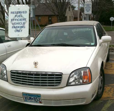 White Cadillac beater parked in a spot marked Reserved fuel-efficent vehicle parking only
