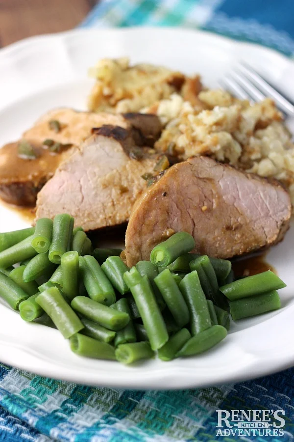 Perfect Pork Tenderloin by  Renee's Kitchen Adventures slices with gravy and green beans on a white plate ready to eat