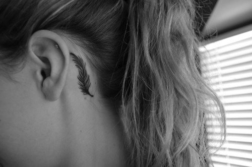 Chica mostrando su tatuaje en forma de pluma de ave que está atrás de su oreja