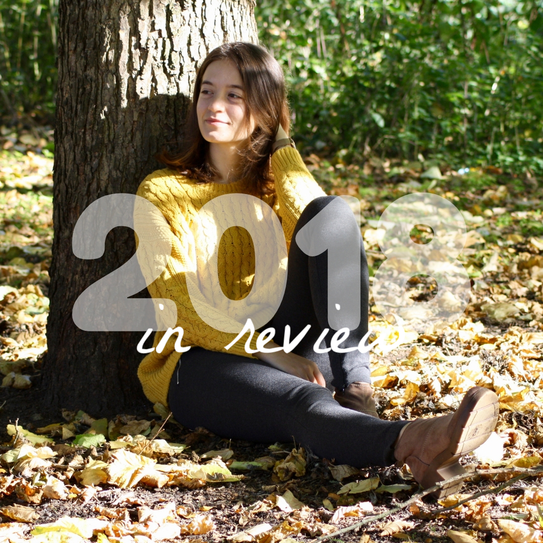 abbey sits at the foot of a tree, surrounded by autumn leaves, looking to the side of the camera
