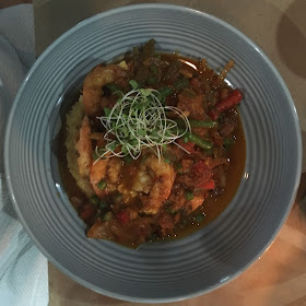 reddish colored grits topped with shrimp and sprouts in a gray bowl