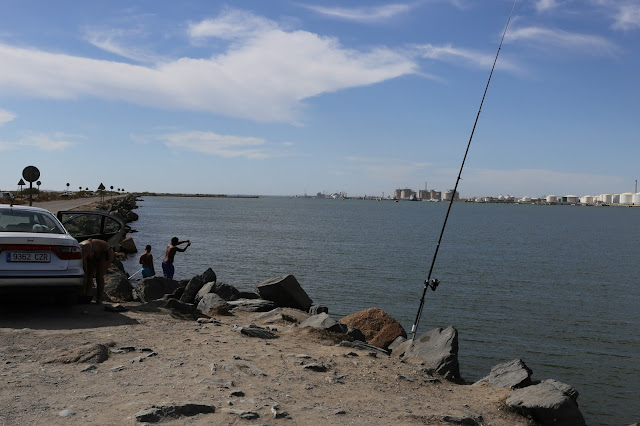 Personas pescando en una estructura artificial de piedra que se adentra en el mar.