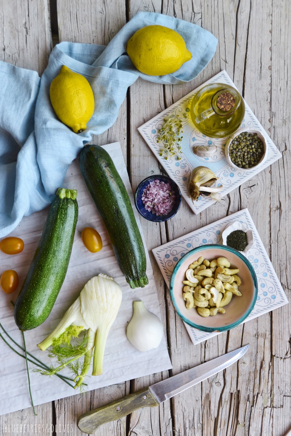 Ingredients for chilled raw soup, zucchinis, lemon, sprouts, cashew nuts on flat lay with light blue linen tablecloth