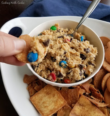 Monster cookie dip is a super fun snack for all of the monster cookie lovers in your life. It is kind of like getting permission to eat cookie dough. Plus you can use fun dippers to do it! Put this on your must make list for your next get together. hand cookie into peanut butter oatmeal and chocolate chip dip