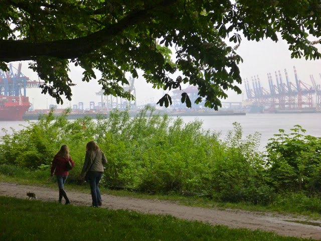 Blick auf Spaziergängerinnen im Grünen, im Hintergrund scheint der Hamburger Hafen durch