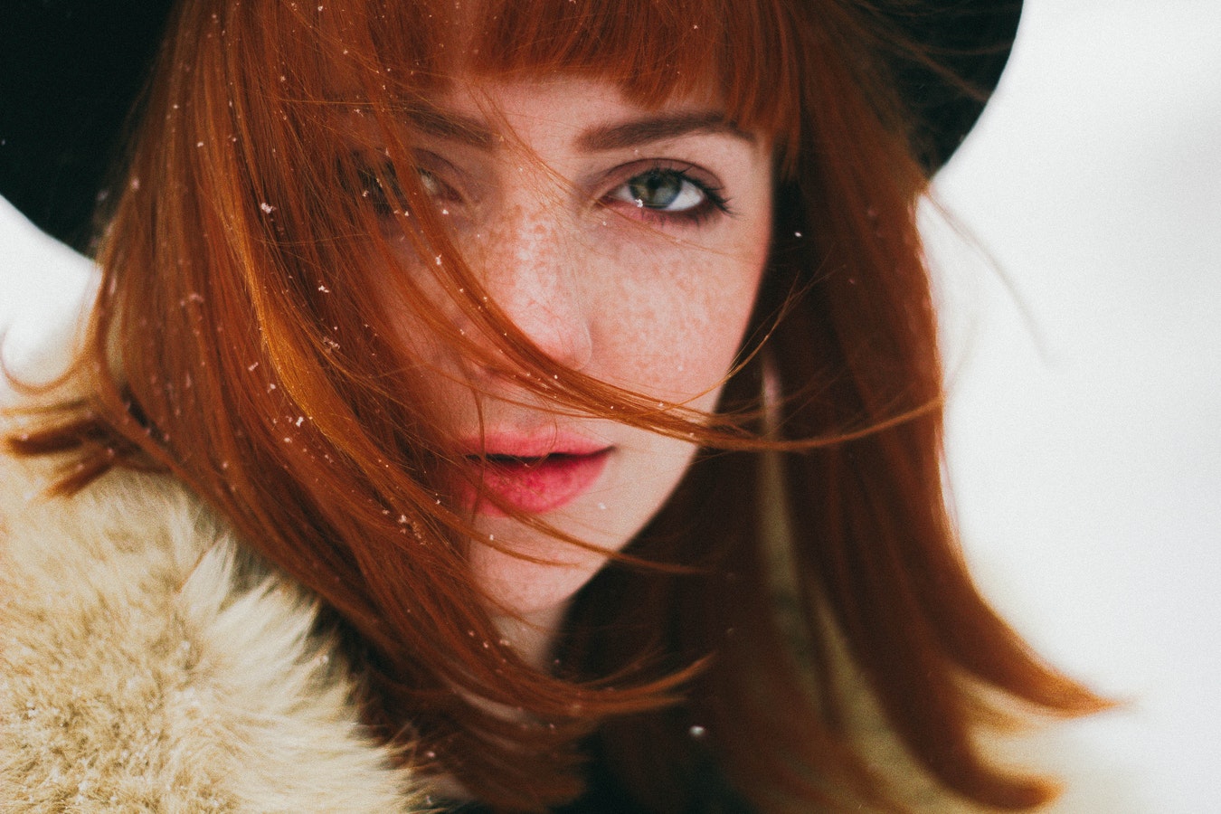 ginger girl with pale skin and freckles in black hat and fur coatat winter