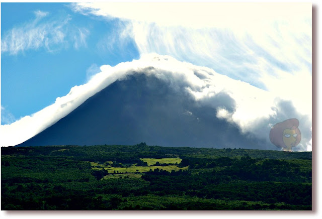Montanha o Pico, a maior de Portugal com 2351m de altitude, Ilha do Pico, Açores, envolta em névoa e nuvens num dia de sol, com o verde da pastagem aos seu pés.