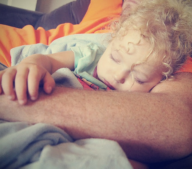 Kind schläft im Arm der Eltern