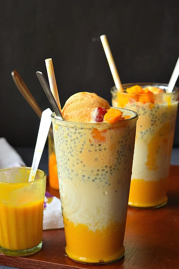 Tall glass holding Mango Falooda - layers of sabja,mango pulp,mango chunks,milk and mango icecream
