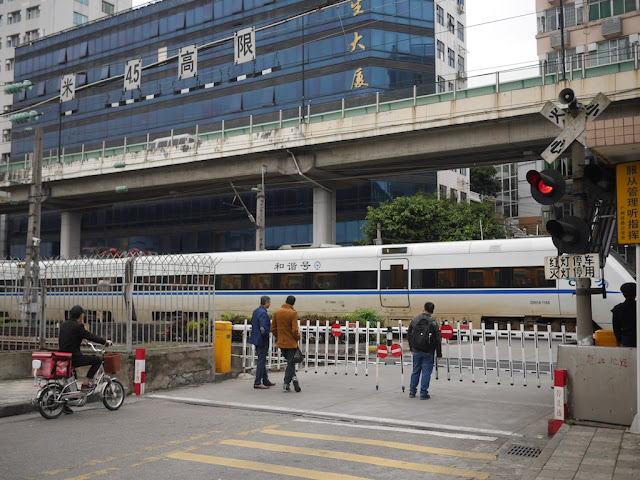 people at a railroad crossing waiting for a high-speed train to pass