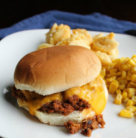 sloppy joe sandwich with melted cheddar cheese on it, macaroni and cheese and corn in the background