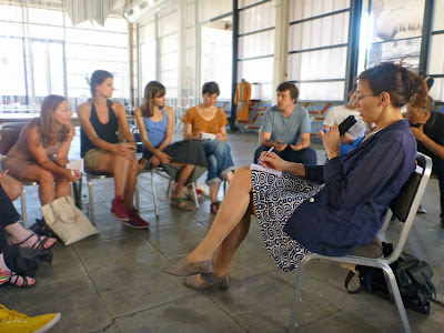 Dolmetscherin mit Mikrofon inmitten einer diskutierenden Gruppe, die auf Stühlen im Kreis sitzt. 
