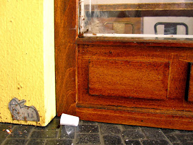 Modern dolls' house miniature cafe exterior detail showing rubbish on the footpath and a paste-up on the wall.