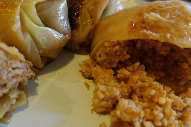 Rolled up parcels of white cabbage, one is cut open with a rice and pork mixture tumbling out on to a white plate