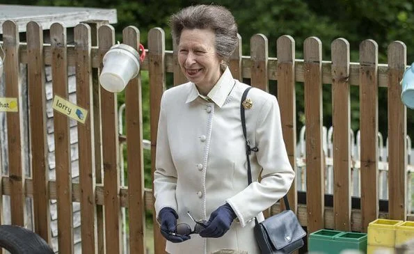 Anne is wearing a cashmere jacket and gold ribbon brooch. She has paired the brooch with a diamond pearl and gold earrings