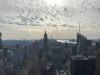 View looking out over New York City on a slightly cloudy day. Empire State Building is in the centre.