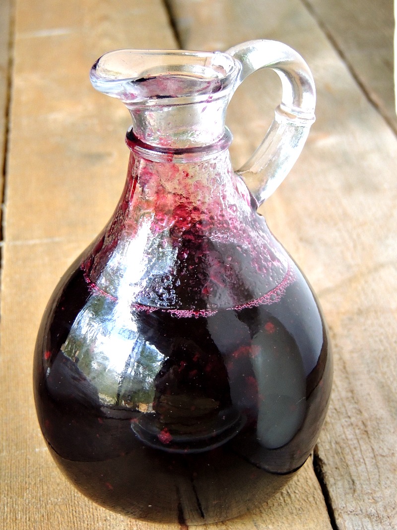 Glass bottle filled with Homemade Blueberry Syrup in it on a wooden table.
