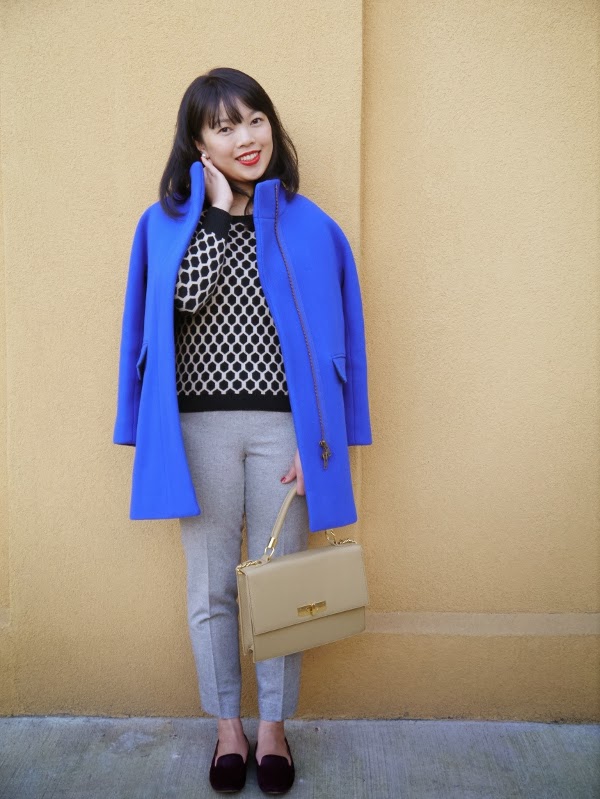Cobalt blue cocoon coat worn with graphic black-and-white sweater, grey ankle trousers, burgundy pony hair smoking slippers, and a structured top-handle bag.