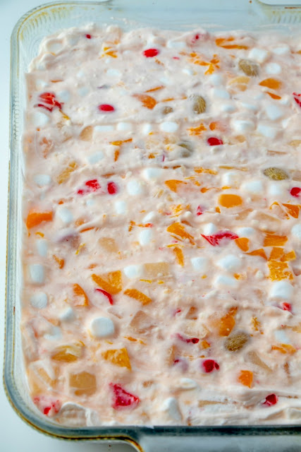 Frozen fruit salad is a blast from the past. This vintage recipe is a cool and delicious way to eat your fruit. It is at home at all of our holiday meals, but would also be a fun summer side dish! looking across a glass pan of frozen fruit salad with bits of fruit cocktail and marshmallows showing