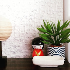 One-twelfth scale Japanese-themed display on a chest of drawers, with a rice-paper lamp. a kokeshi dolls, a plant in a blue-and-white Japanese pot and a white rectangular bowl.