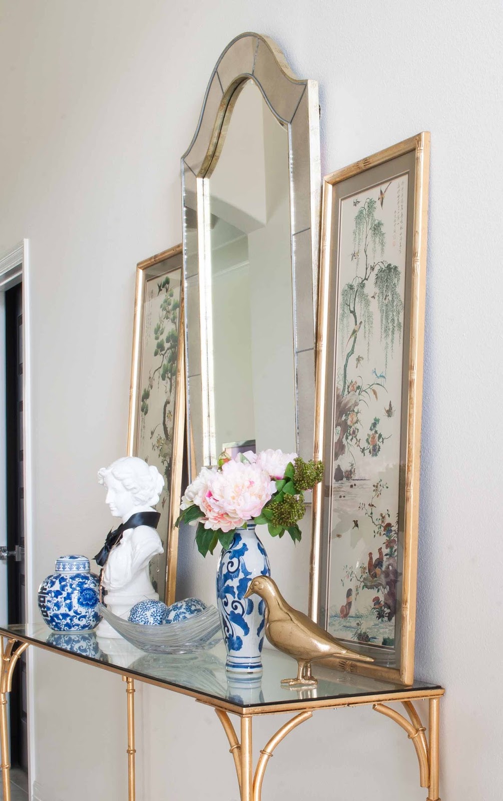 Chinoiserie ginger jars, flowers, vintage art and a gold bamboo console table in a foyer. Chinoiserie ginger jars, flowers, vintage art and a gold bamboo console table in a foyer.