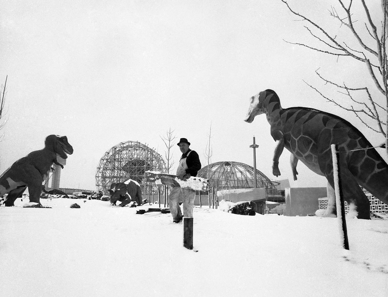 Carpenter Henry Johnson doesn't seem to concerned about his clutch of prehistoric companions at the Sinclair Oil Exhibit in the World's Fair grounds, New York City, February 19, 1964. The Ferris wheel-like contraption behind Johnson to the right is the U.S. Rubber Exhibit.