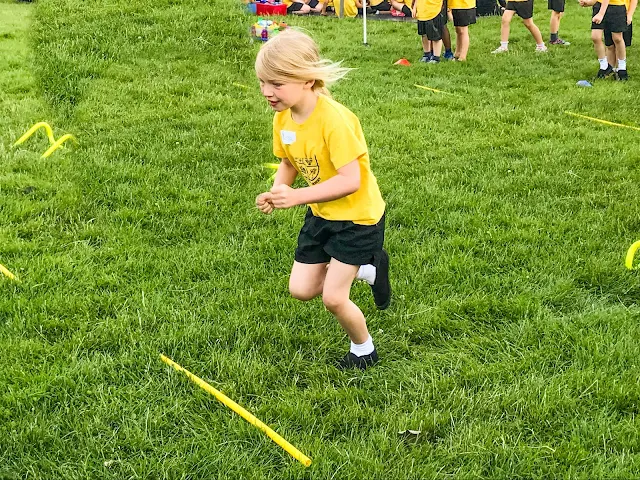 A young girl running in a hurdles race over small yellow bits of plastic