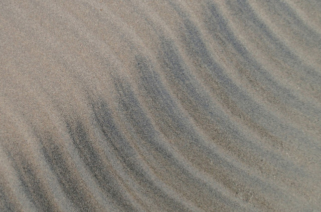 Aallokon tekemiä raitakuvioita hiekassa.
