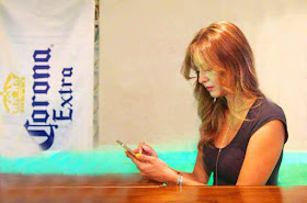 Beautiful girl looking at cell-phone, Corona Beer sign, bar