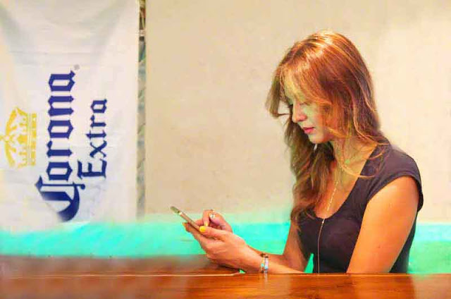 Beautiful girl looking at cell-phone, Corona Beer sign, bar