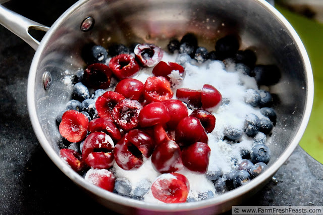 freshly pitted cherries in a saucepan with sugar and blueberries