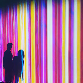 Shadows of two people against an artwork made up of many colourful stripes.
