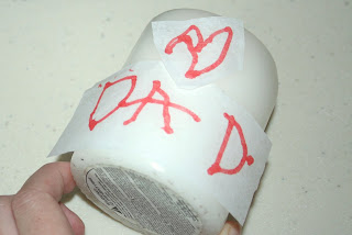 Pieces of paper that spell out "dad" on a white candle to design their own candle