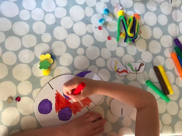 A cardboard ladybird being coloured in red and purple