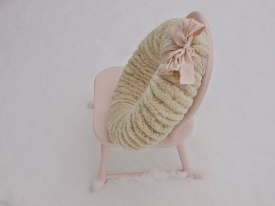 Woolly white handmade pom pom wreath with pink ribbon on pink chair in snow