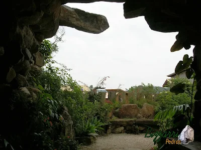 Detalhe da construção da gruta de pedra, com pedra moledo, de dentro para fora, com o banco de pedra, o piso de pedrisco e a execução do paisagismo.