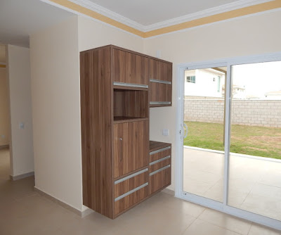 A cozinha conta com marcenaria completa, com gaveteiros e nichos para fornos de microondas e elétrico. Na esquerda fica o acesso para a sala de jantar, que também se comunica com a varanda gourmet à direita.