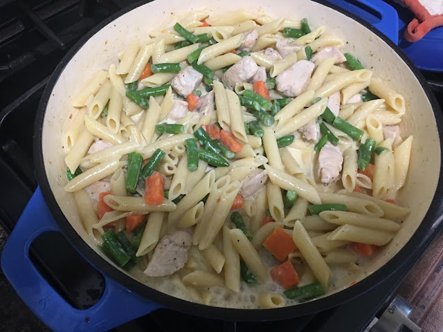 The creamy chicken and vegetable pasta in the pan on the stove. 