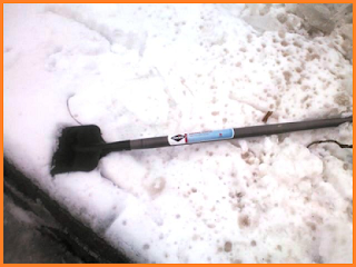 Ice chisel with black blade and gray handle sitting on snow