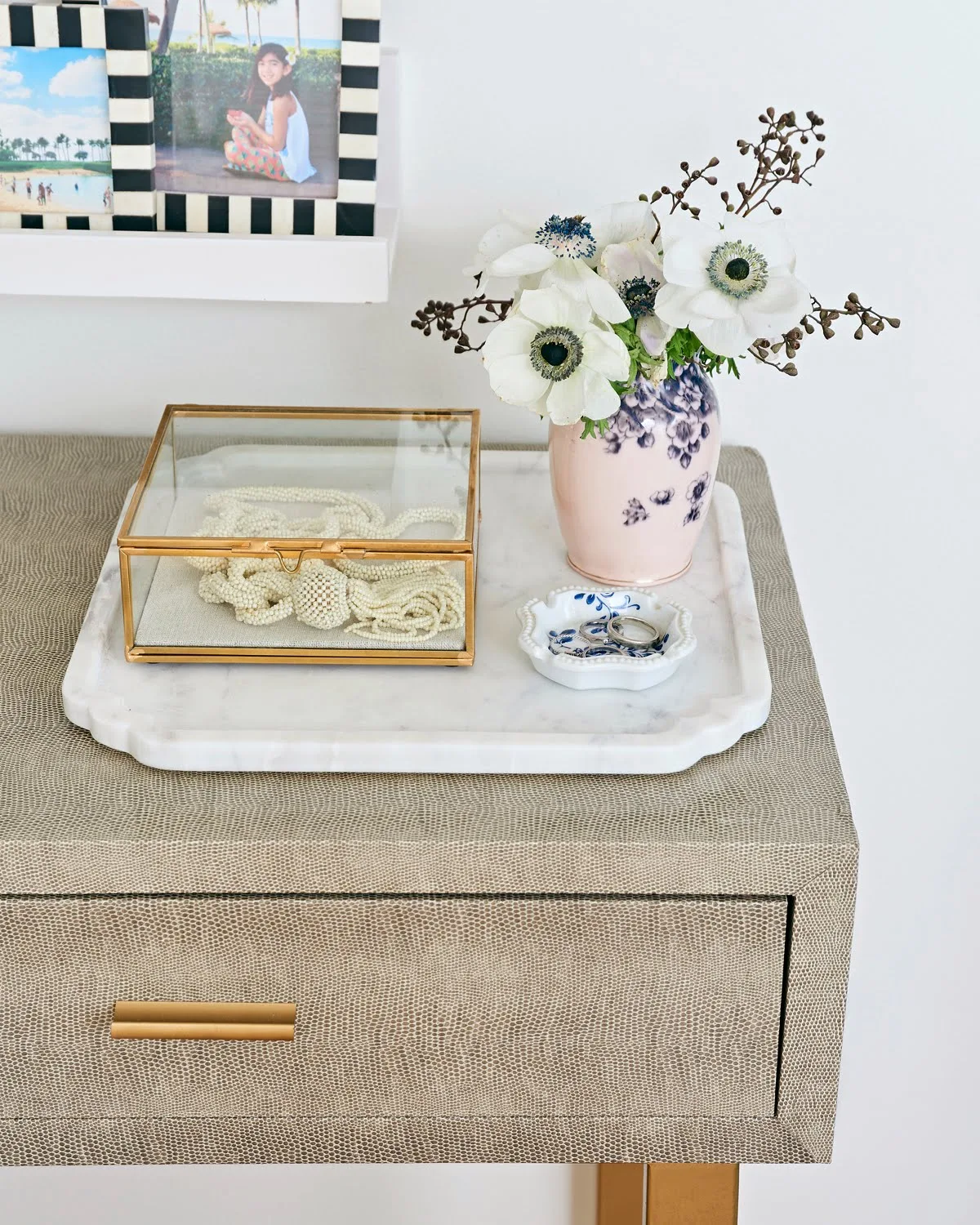 black and white frames with family photographs, a vase with anemones, gold glass box on marble tray