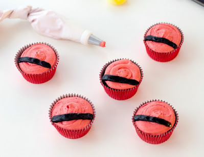 piping belt onto cupcakes red frosted cupcakes with black stripe of frosting across them for belt