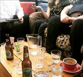 Group of people sitting around a coffee table filled with various drinks and glasses.