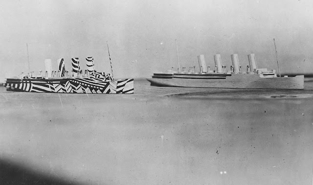 Once painted, the camouflaged ships would be placed on a tabletop to be viewed through a periscope, simulating conditions at sea, to evaluate the effectiveness of the patterns. Original caption: Models of two ships on same line of direction, one plain, and the other dazzled. This method of camouflage was used on battleships and transports to deceive U-Boat commanders and make correct aim difficult.