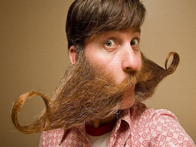 Homem jovem com barba e bigode em formatos muito exótico ou bizarro.