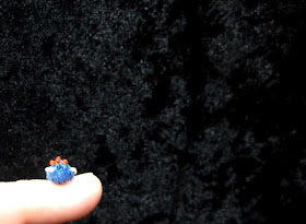 Tiny hand-knitted tea cosy balanced on a pinky fingernail