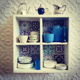 Modern miniature white wall shelf with blue and white tiles on the back, filled with blue and white crockery and with various jugs displayed on the top.