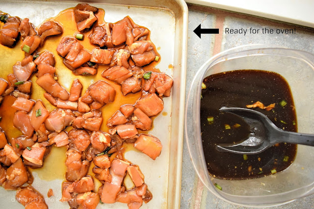 Marinated chicken pieces are on top of a baking sheet ready to go to the oven. A bowl of used marinade and a large spoon are on the side. 