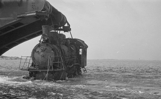 A barge lifts a wrecked locomotive.