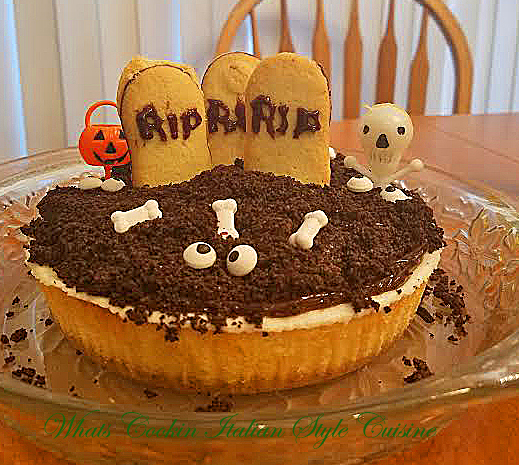 this is a scary looking Halloween grave yard cheesecake with crushed oreo cookies on top, bones, eyes and pumpkins on top along with grave yard milano cookies with tombstone messages on them a ghoulish treat for Halloween party fun thats delicious the cheesecake is a homemade recipe from scratch from my hometown Utica New York