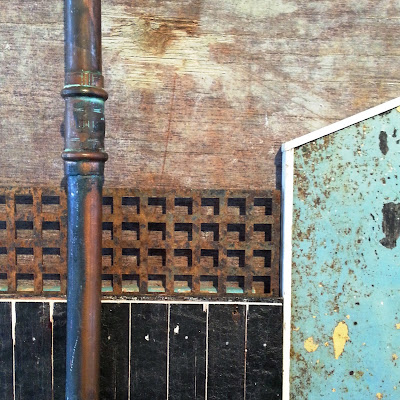 Detail of an assemblage art piece by Alex Asch, made up of various pieces of distressed board, pipe and metal.